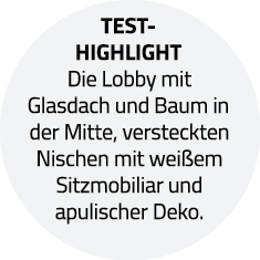 Test-Highlight Die Lobby mit Glasdach und Baum in der Mitte, versteckten Nischen mit weißem Sitzmobiliar und apulisch   